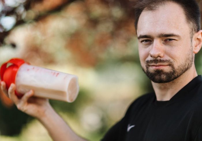 Adult man holding a protein shake outdoors during the day.